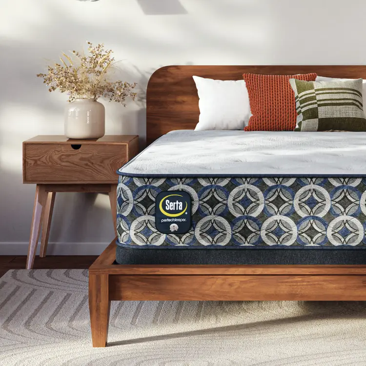 Serta Perfect Sleeper plush mattress on a wooden bed with decorative pillows and a nightstand in a bedroom setting.
